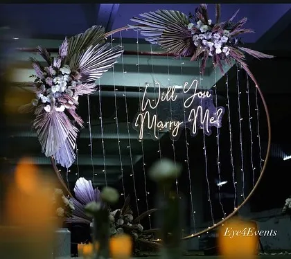A dreamy, softly lit view of our boho-chic proposal ring. The combination of dried palm leaves, white flowers, and cascading fairy lights creates a whimsical and romantic setting.