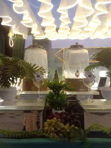 A beautiful daytime setup for a welcome drink station. It features two large glass dispensers with fresh juices or iced tea, decorated with lush greenery for a refreshing look.