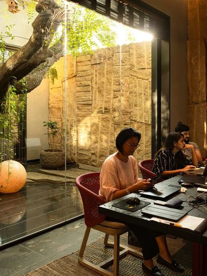 A biophilic workspace where employees work next to a glass-enclosed courtyard. The design brings a mature tree and natural light into the office, creating a calm and inspiring environment that enhances focus and well-being.