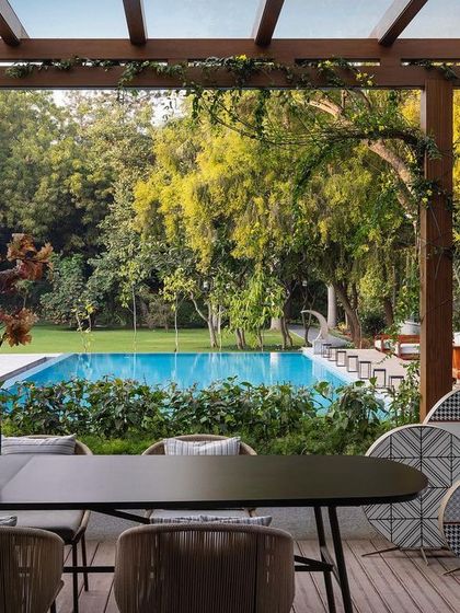 An outdoor dining area on the wooden deck, overlooking the pool and expansive lawn. The space is perfect for alfresco meals, surrounded by meticulously landscaped gardens.