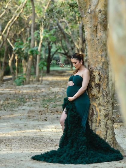 A quiet, reflective moment captured during an outdoor shoot. The expectant mother leans against a tree, cradling her belly, creating a serene and personal maternity portrait.