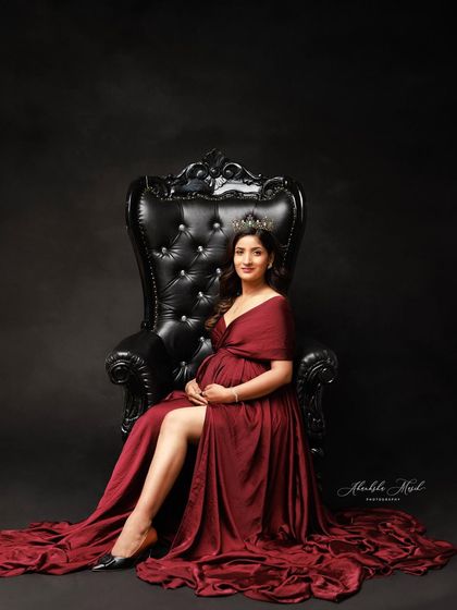Seated on a throne-like chair, this mother-to-be exudes power and grace in a deep red gown and crown.