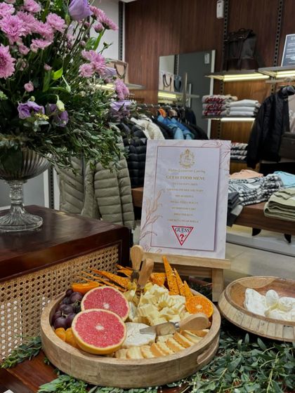 A beautifully arranged cheese board for the GUESS Autumn/Winter collection launch. The platter includes grapefruit, grapes, and a selection of fine cheeses, set against a backdrop of lush florals.