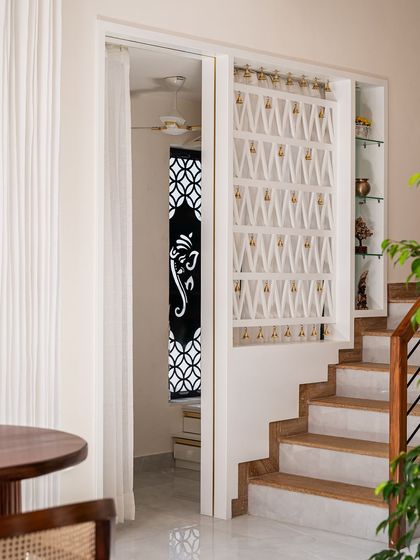 Adjacent to the staircase, I designed this puja room wall with CNC-cut partitions. The intricate geometric pattern adds a traditional touch to an otherwise modern space, and the bells inside add a sensory detail.