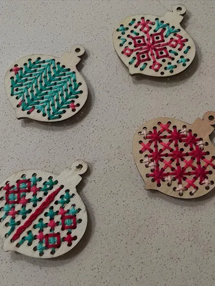 A closer look at the hand-embroidered wooden ornaments. The pre-drilled holes guide the stitches, making this a great project for beginners or children.