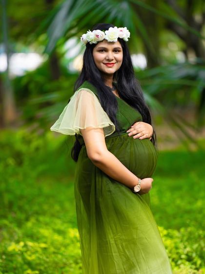 A beautiful solo portrait in a garden. The mom-to-be, in a green ombre dress and floral crown, looks radiant and serene among the trees.