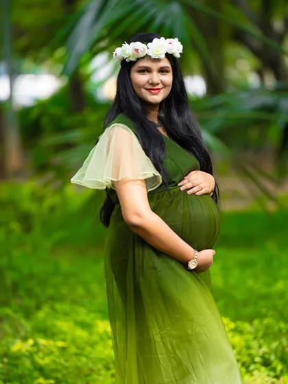 A beautiful solo portrait in a garden. The mom-to-be, in a green ombre dress and floral crown, looks radiant and serene among the trees.