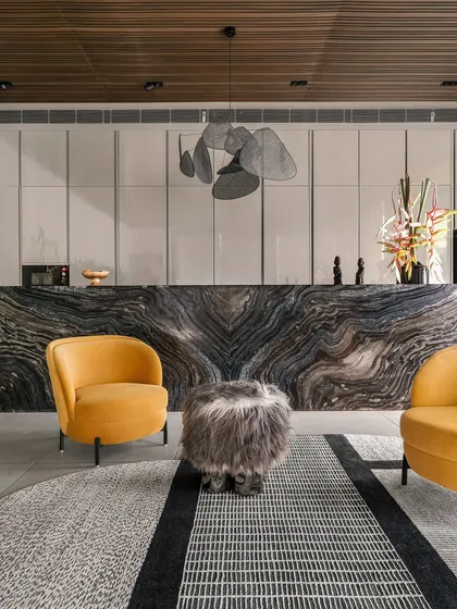 The heart of the pool house is this dramatic bar counter, crafted from a single piece of book-matched marble with incredible natural veining. Paired with bold mustard armchairs and a sculptural pendant light, it becomes a functional work of art.