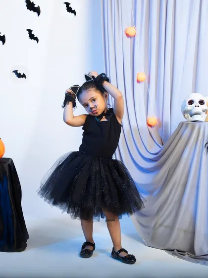 Showcasing a different product from the same brand, this is a full shot of a child's cat costume. The model's playful pose and the carefully arranged Halloween background create a fun, energetic image that effectively markets the product for party or event wear.
