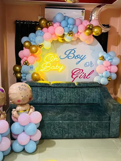 A fun "Oh Boy or Girl?" gender reveal party setup. The decor includes a custom backdrop, pink and blue balloon garlands, and cute baby-shaped foil balloons.