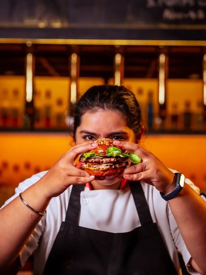 A chef holds up our classic Oklahoma-style smashed beef onion burger, a juicy, multi-layered culinary experience.