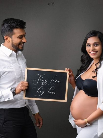 A stylish maternity portrait with the couple holding a sign that reads "Tiny toes, big love".