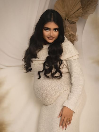 A portrait of glowing anticipation. The mother-to-be, dressed in a soft, neutral-toned dress, looks directly at the camera with a gentle confidence. The bohemian-inspired backdrop adds a touch of warmth.