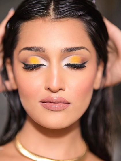 A close-up of the bold, golden glam look. The sharp contrast between the yellow, white, and black liner creates a striking and modern graphic eye.