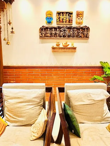 A seating area with traditional wooden chairs, carved pillars, and a wall adorned with ethnic masks and carvings.