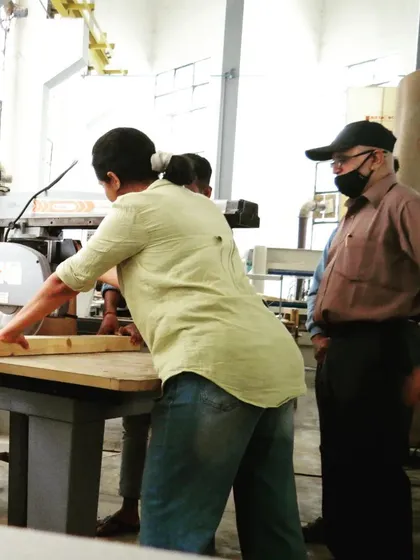 Under the watchful eye of an instructor, a student uses the radial arm saw to make accurate crosscuts on a long piece of timber.