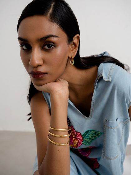 A portrait that highlights both earrings and bracelets. The model's pose, with her chin resting on her hand, naturally brings the stacked gold bangles into the frame.