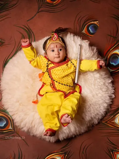 Celebrating Janmashtami with our own little Kanha. This vibrant top-down shot captures the playful spirit of the festival, with a peacock feather backdrop and traditional attire for a unique cultural baby photoshoot.