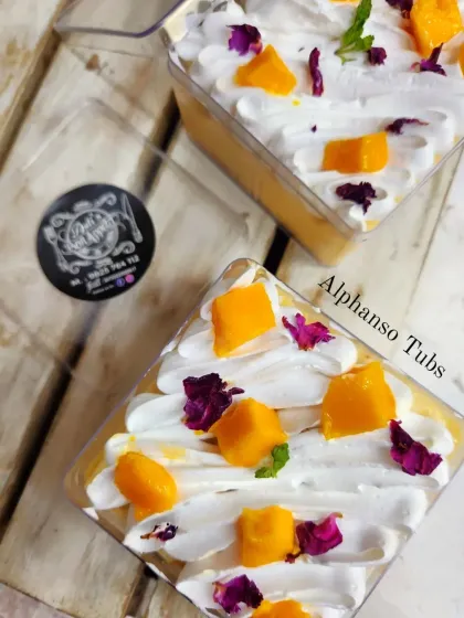 These individual Alphonso Mango Tubs are a perfect single-serving dessert. They feature layers of light cake, whipped cream, and fresh mango puree, topped with mango chunks and edible flowers.
