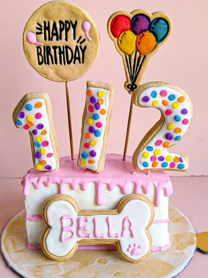 Bella's half-birthday cake is a mini version of our larger designs, complete with a pink drip, a personalized bone, and "1/2" number cookies.