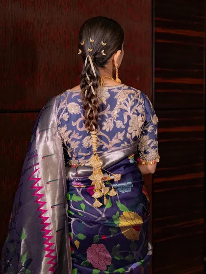 The hairstyle is a work of art. This sleek choti is adorned with classic Maharashtrian hair accessories, including the crescent moon clips, adding a touch of redefined elegance.