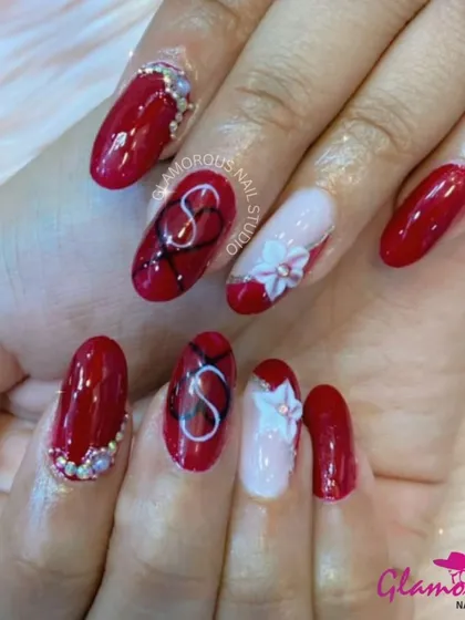 A sophisticated design combining classic red with delicate 3D art. This set features glossy red nails, a custom initial design, and a beautiful, hand-sculpted white flower, all accented with tiny rhinestones for a touch of sparkle.