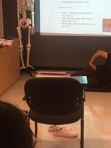 Correcting form is crucial. Here, a trainer adjusts a student's posture during a demonstration of a core exercise, linking theory to practical application.