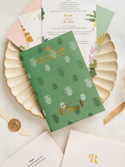 A sophisticated invitation suite with a green patterned folder featuring gold-foiled Gujarati script. This design beautifully blends modern aesthetics with traditional language and motifs.