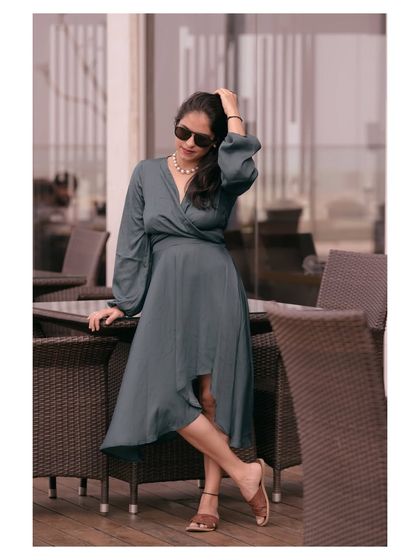 A lifestyle shot of a model in a grey wrap dress at an outdoor cafe. This image tells a story and shows the product in a real-world scenario.