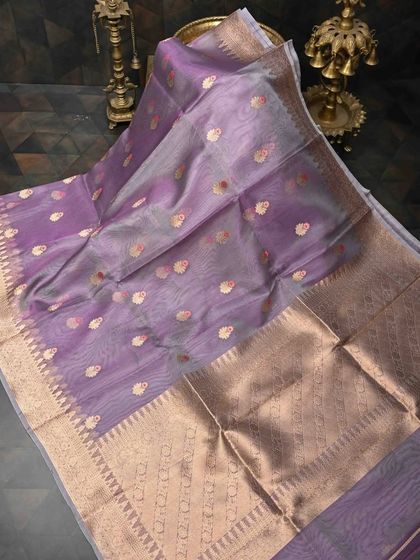 A lovely lavender organza silk saree with gold butis and a wide gold border. The sheer fabric and soft color create an ethereal and elegant look.
