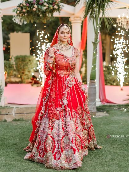 A stunning full-length portrait of the bride in her radiant red lehenga, with the magical sparkle of fireworks in the background.