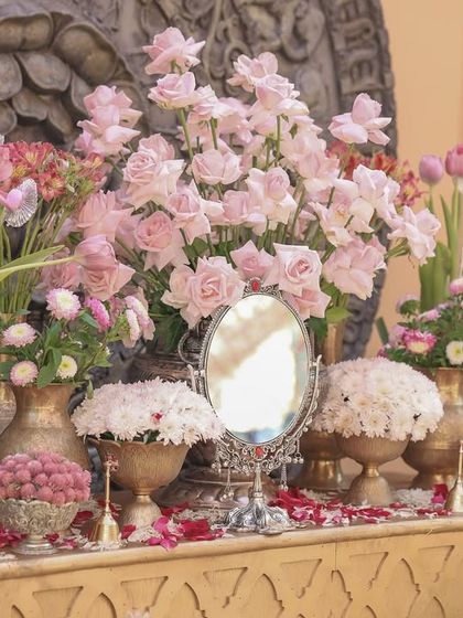 A console table decorated with an array of pink flowers in antique silver and brass vases, along with a vintage mirror, creating a look of royal elegance.