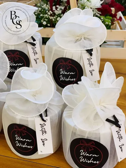 Small jars elegantly wrapped in white fabric, cinched at the top, and tied with a simple black string. The custom "Warm Wishes" and "With Love" tags add a personal and heartfelt touch.
