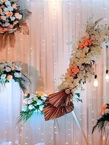 An asymmetrical floral arch in peach and white tones creates a soft and romantic focal point, complemented by hanging Edison bulbs for a warm, ambient light.