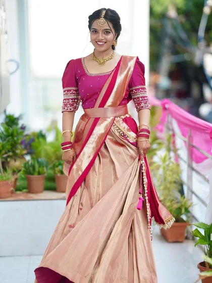 A happy bride showing off her unique pink and gold half-saree. The makeup is radiant and complements the youthful feel of the outfit.