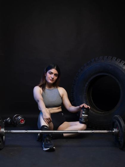 A relaxed post-workout style shot, with the model seated on the floor next to a barbell and the supplement. This image conveys a sense of accomplishment and recovery, targeting customers looking for post-workout nutrition solutions.