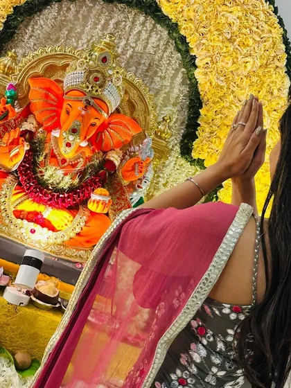 A moment of prayer in front of the vibrant yellow floral Ganpati decor. The color yellow symbolizes happiness, making it a perfect choice for this auspicious festival.