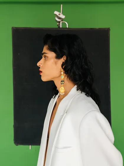 A classic profile portrait for Amama Jewels. The simple composition against the green and black studio background emphasizes the model's silhouette and the featured jewelry.