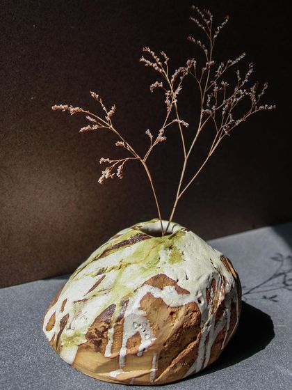 A round, rock like Kurinuki vase holding a delicate sprig, a beautiful contrast of textures and forms.