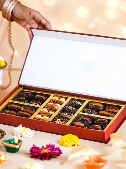 A festive Diwali gift box of assorted dates being presented. The soft, glowing background and traditional elements create a warm and premium feel for holiday gifting.