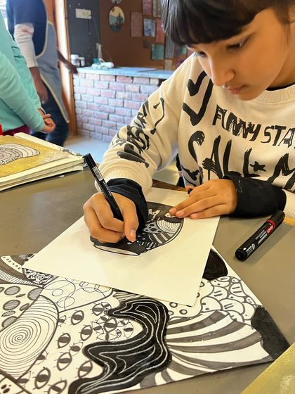 A close-up of a student drawing complex, doodle-like patterns with a fine-tipped marker.