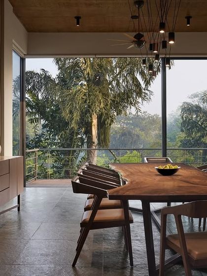 This dining space is designed for timeless gatherings, where elegance meets a natural ambiance. A live-edge wooden table serves as the centerpiece, surrounded by large windows that frame the lush greenery outside, creating a dining experience that feels connected to nature.