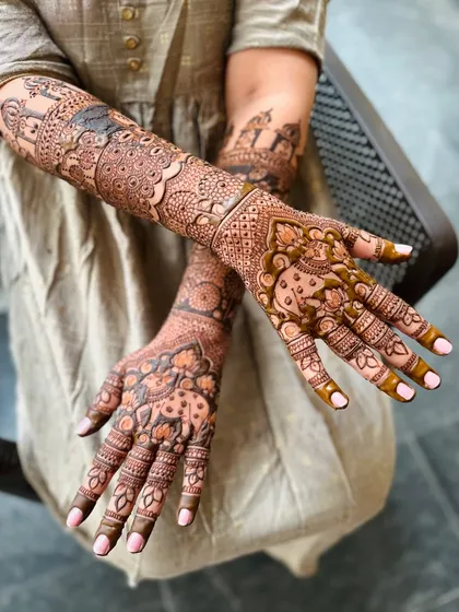 This design tells a story with elephant motifs and traditional symbols, covering the arms from wrist to elbow in a rich tapestry of henna.