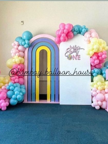 A candy-themed first birthday backdrop with a giant lollipop prop, a rainbow archway, and a large pink number "1".