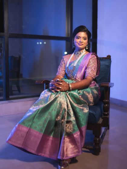 A full-length portrait of the bride in her reception attire. The cool-toned lighting enhances the beautiful colors of her saree, and her makeup looks flawless.
