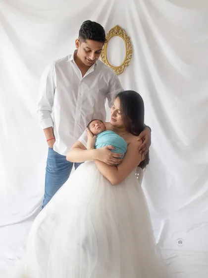 A classic family portrait with their newborn. The mother's flowing white dress and the baby's peaceful sleep create a beautiful and elegant scene.