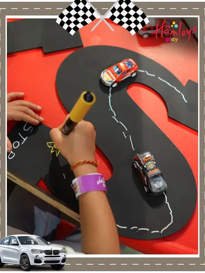 Learning can be fun! At our Mini Racers event, a child practices writing letters by tracing them on a custom-made racetrack, combining playtime with early learning skills.