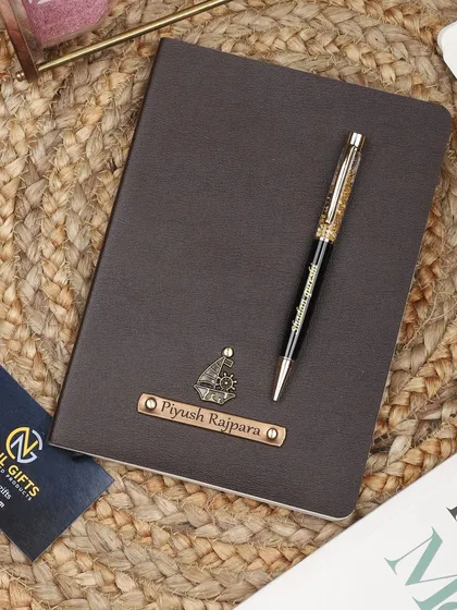 A personalized brown leather diary with a ship charm, paired with a matching gold flake pen. The diary is shown on a rustic jute mat.