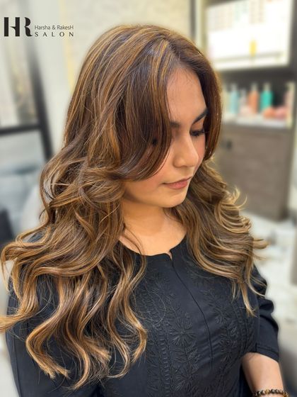 A client portrait showcasing her new balayage with face-framing highlights and a bouncy blowout.