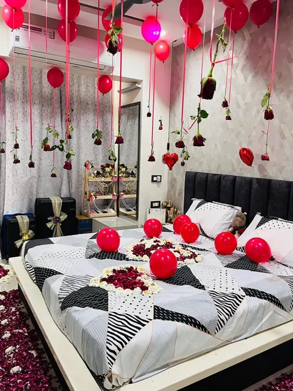 I focus on the small details that make a big difference. Here you can see the intricate heart-shaped art I create on the bed using red and white rose petals, surrounded by more balloons. Real red roses and heart ornaments hang from the ceiling, adding a touch of elegance to the romantic setup.